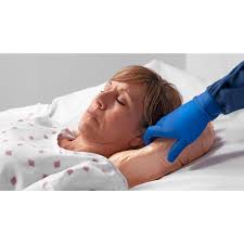 A person lying in a bed with a blue-gloved hand touching their head, in a clinical indoor setting.